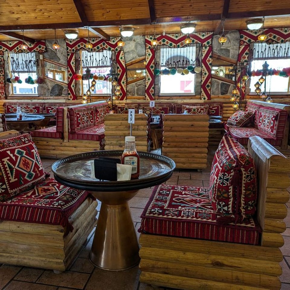 Majeed Mediterranean Restaurant interior with log furniture, red patterned cushions, and decorative lighting.