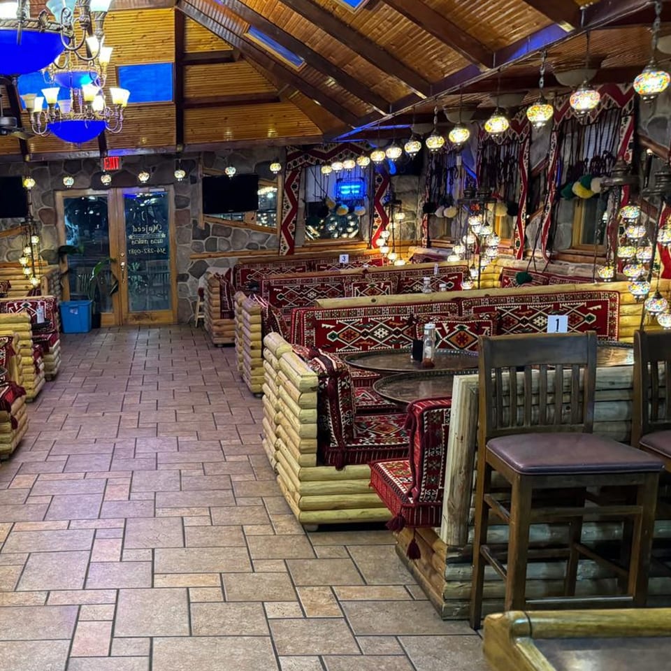 Interior of Majeed Mediterranean Restaurant with patterned red seating, wooden tables, and ornate hanging lamps.