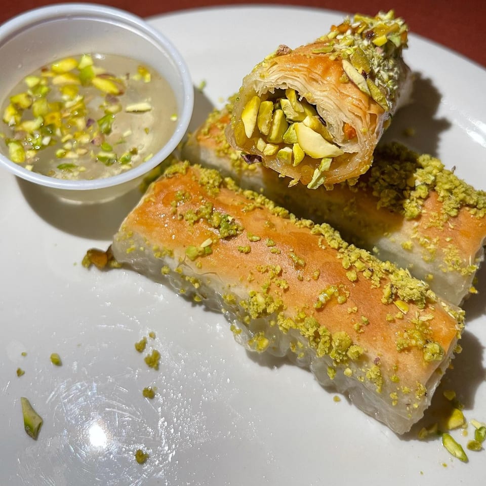 Three pieces of baklava, one standing upright, filled with pistachios and served with syrup.