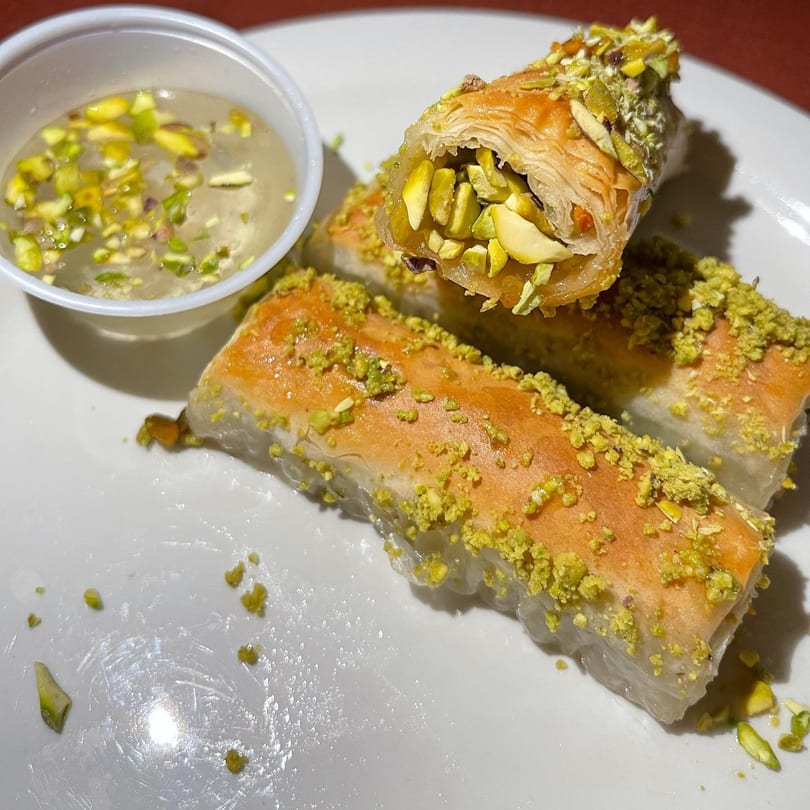 Three pieces of baklava, one standing upright, filled with pistachios and served with syrup.