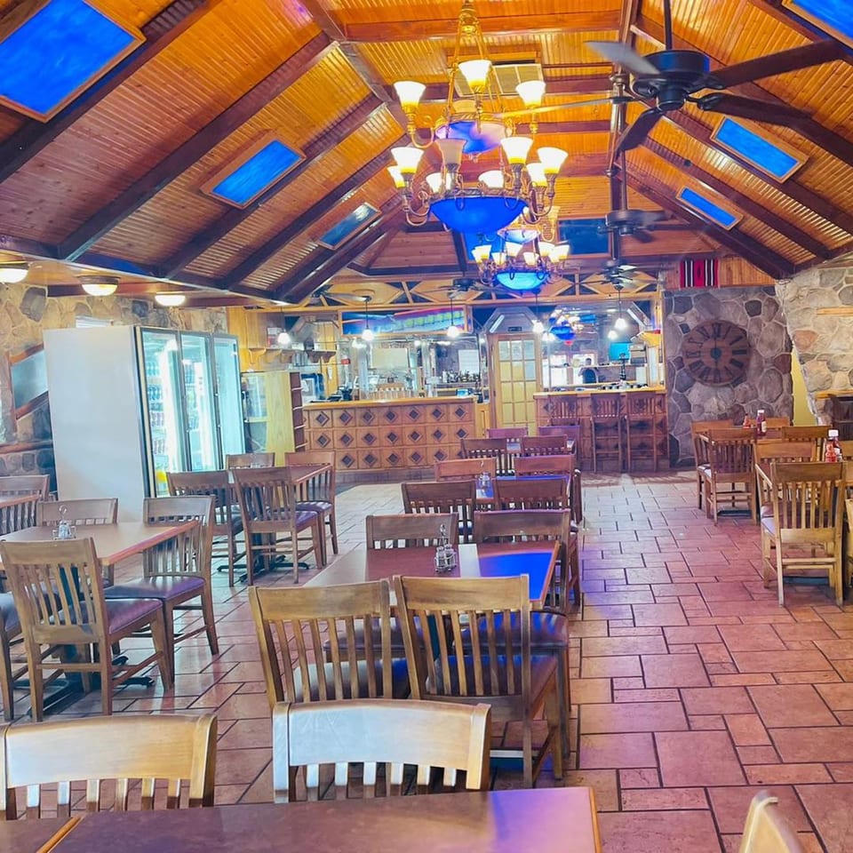 Interior of Majeed Mediterranean Restaurant with wooden tables and chairs, stone walls, and a high wooden ceiling.