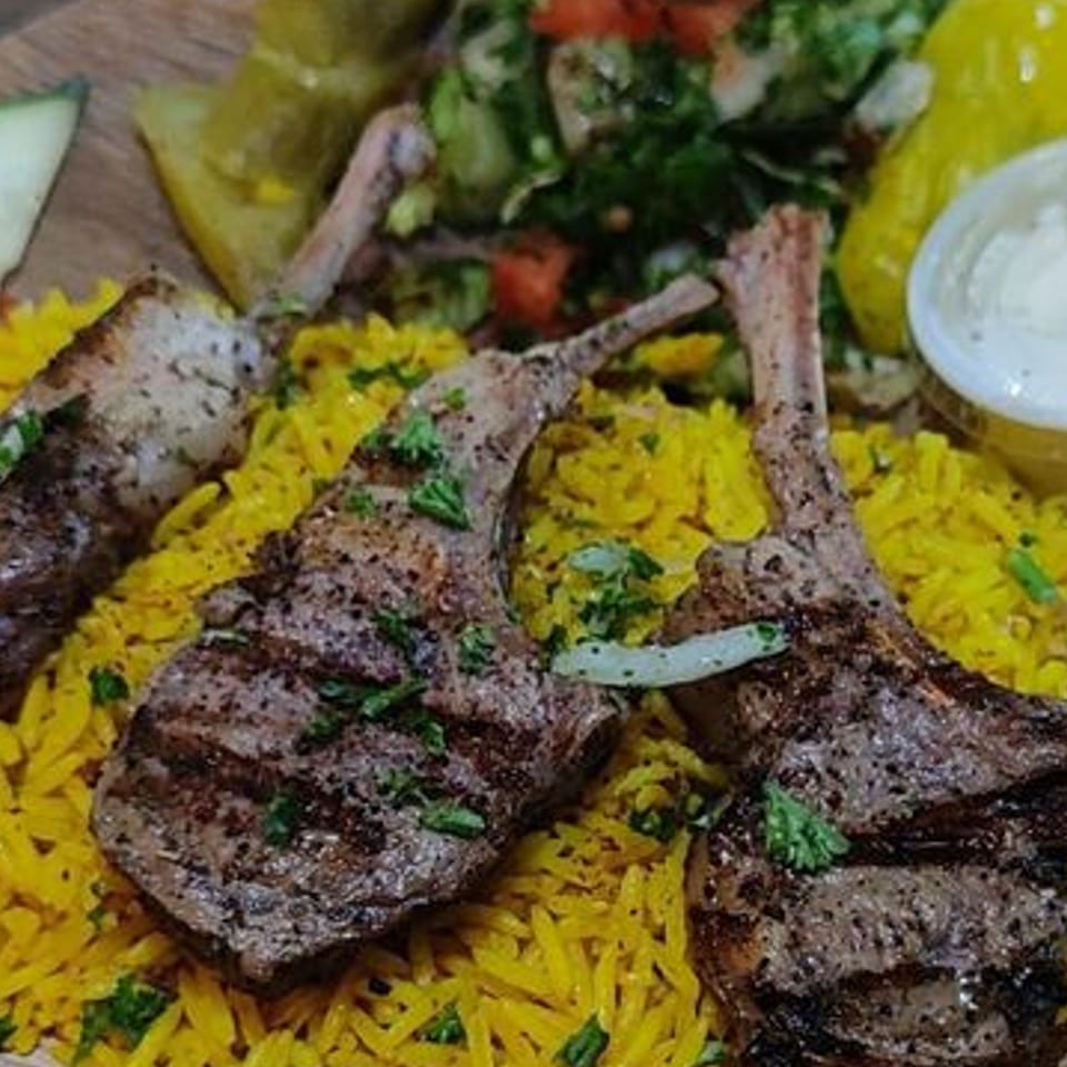 Grilled lamb chops on a bed of yellow rice, with a side of salad and sauce.
