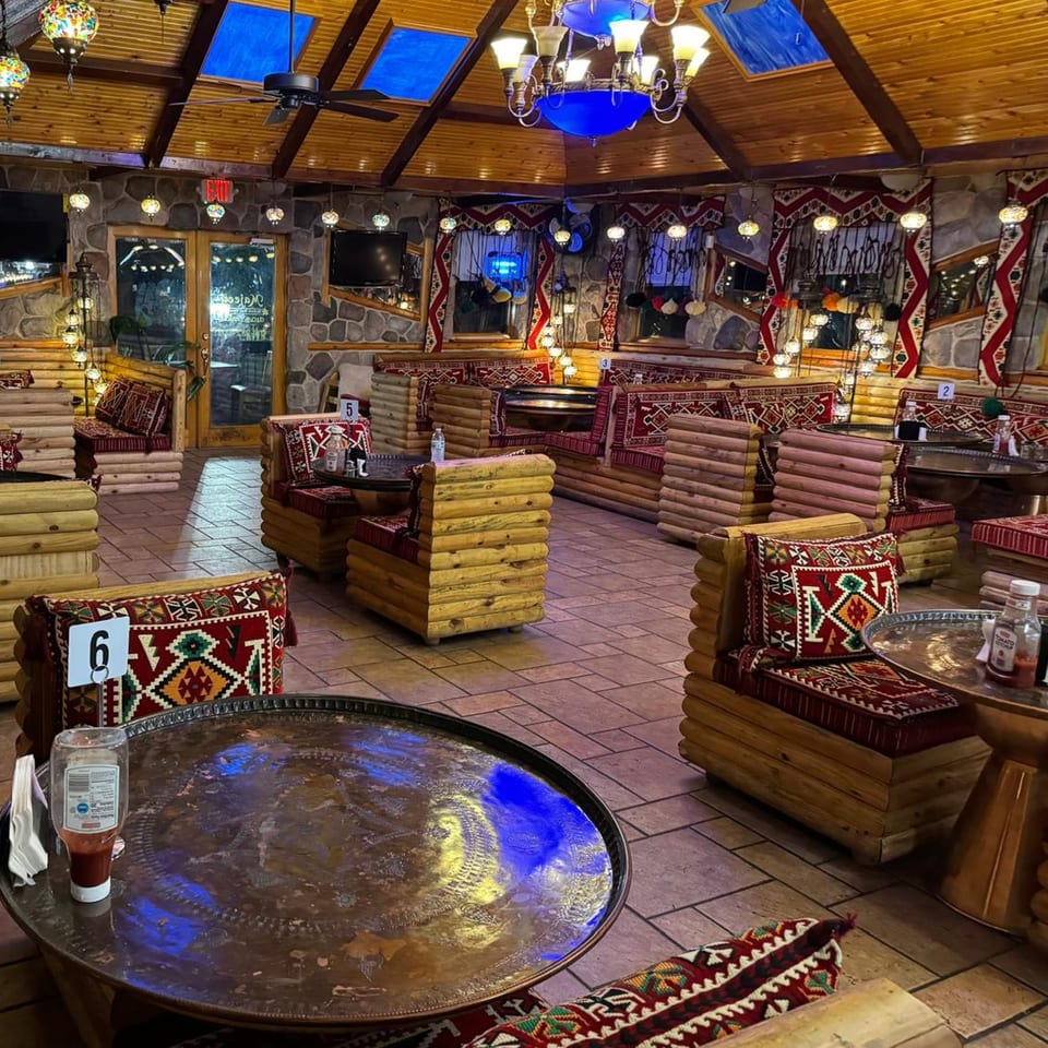Cozy Mediterranean restaurant interior with log seating, patterned cushions, and ornate hanging lamps.