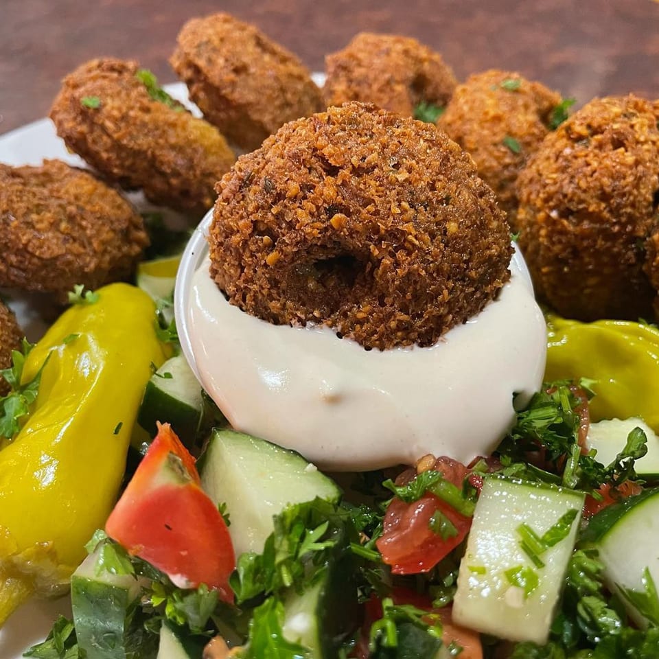 Crispy falafel balls with creamy white sauce, fresh salad, and yellow peppers.